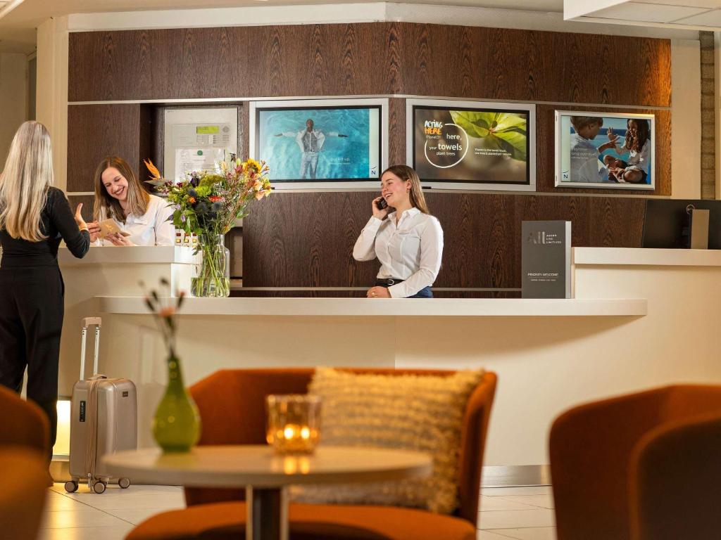 two women standing at a counter talking on a cell phone at Novotel Maastricht in Maastricht