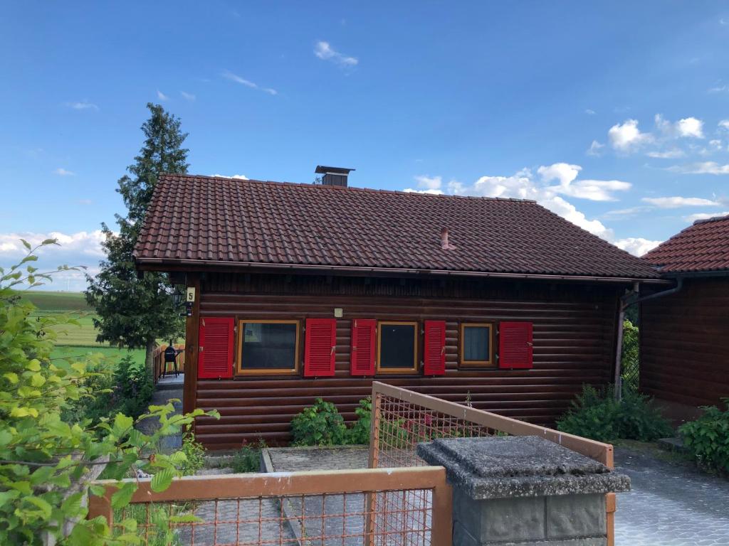 a log house with red shutters and a fence at Bahnhöfle Ferienhaus in Stubersheim