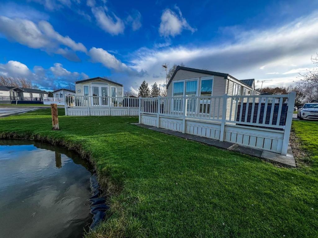 a house with a fence next to a pond at Great Caravan For Hire With Pond Views At Manor Park Holiday Park Ref 23228k in Hunstanton