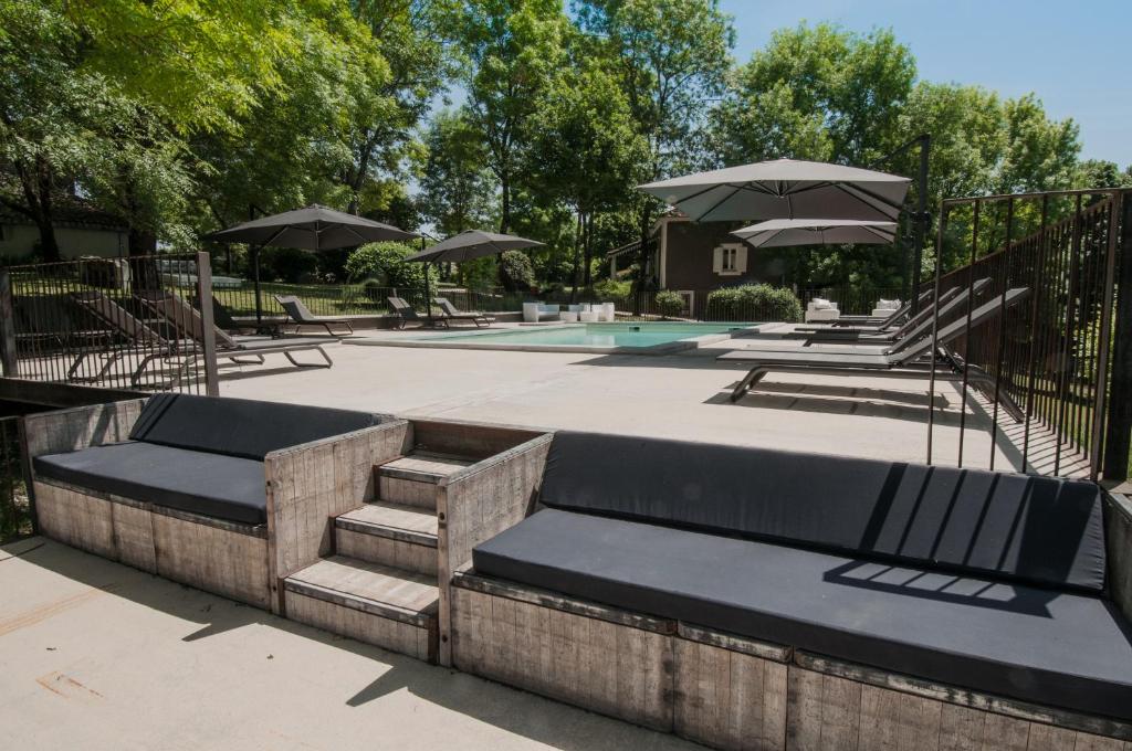 a patio with benches and umbrellas next to a pool at Bassiviere Barn Chic in Saint-Étienne-de-Villeréal