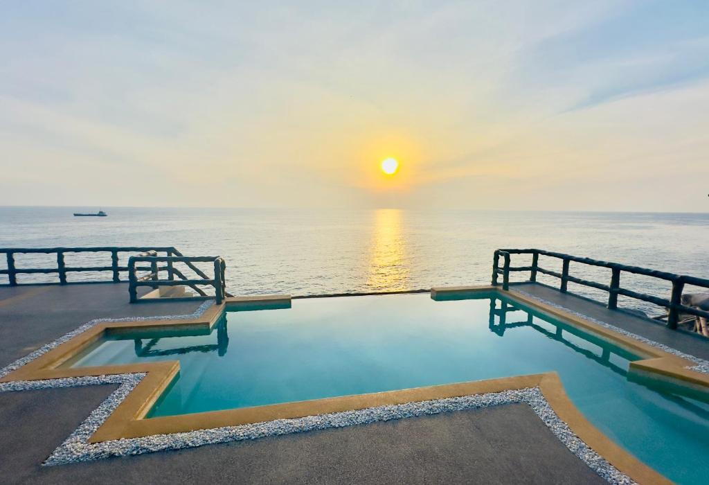 a swimming pool in front of the ocean at sunset at Ocean Front Apartments in Koh Tao