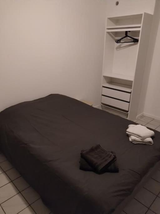 a bed with a black blanket and two towels at Confortable appart 5 mins centre de valenciennes in Anzin