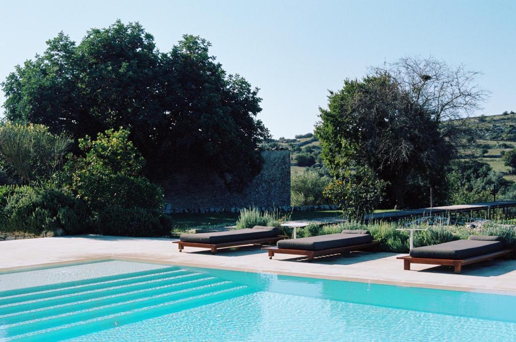 una piscina con due panche e un tavolo accanto ad essa di Dimora delle Balze a Noto