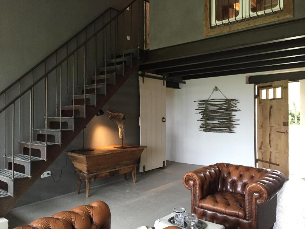 a living room with a staircase and a leather chair at Bassiviere Barn Chic in Saint-Étienne-de-Villeréal