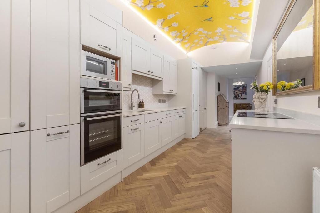 ロンドンにあるStylish Kensington Courtyard Apartmentの白いキャビネットと黄色の天井が備わるキッチン