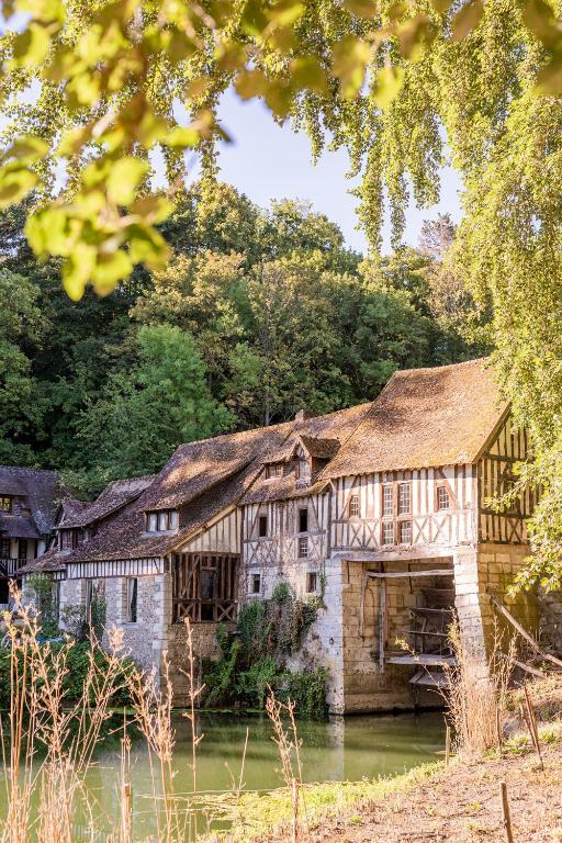 une maison ancienne avec un toit de chaume sur une rivière dans l'établissement Le Moulin d'Andé, à Andé