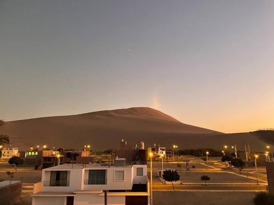 uma montanha à distância com um edifício num parque de estacionamento em La Duna de Emy em Ica