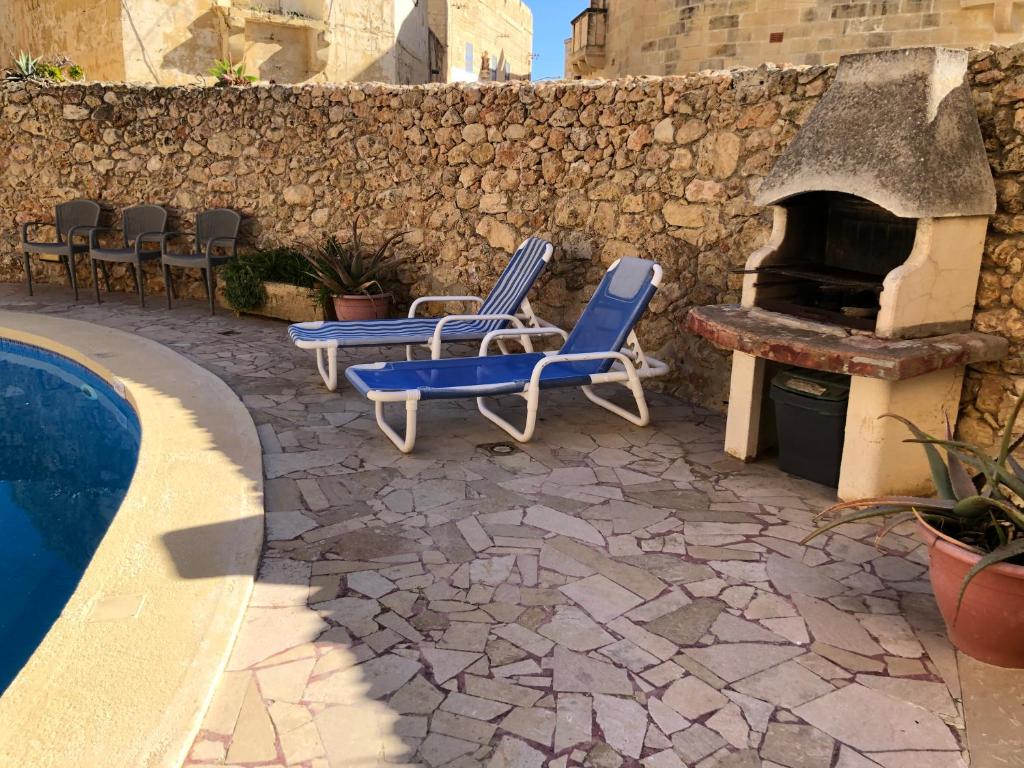 a patio with two chairs and a fireplace next to a pool at Gozo Silence in Għarb
