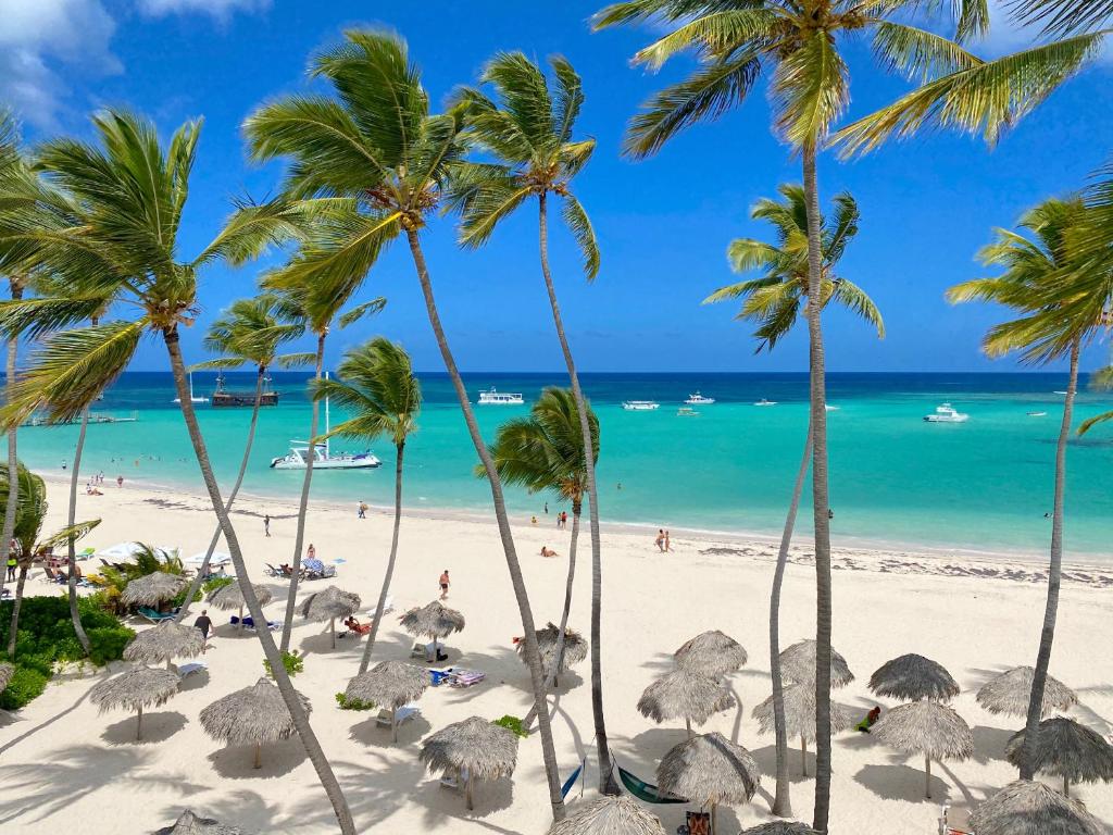 a beach with palm trees and people on the beach at Sunny Seascape Villas & Aparts Hotel WiFi BBQ Los Corales BAVARO BEACH Club & spa in Punta Cana