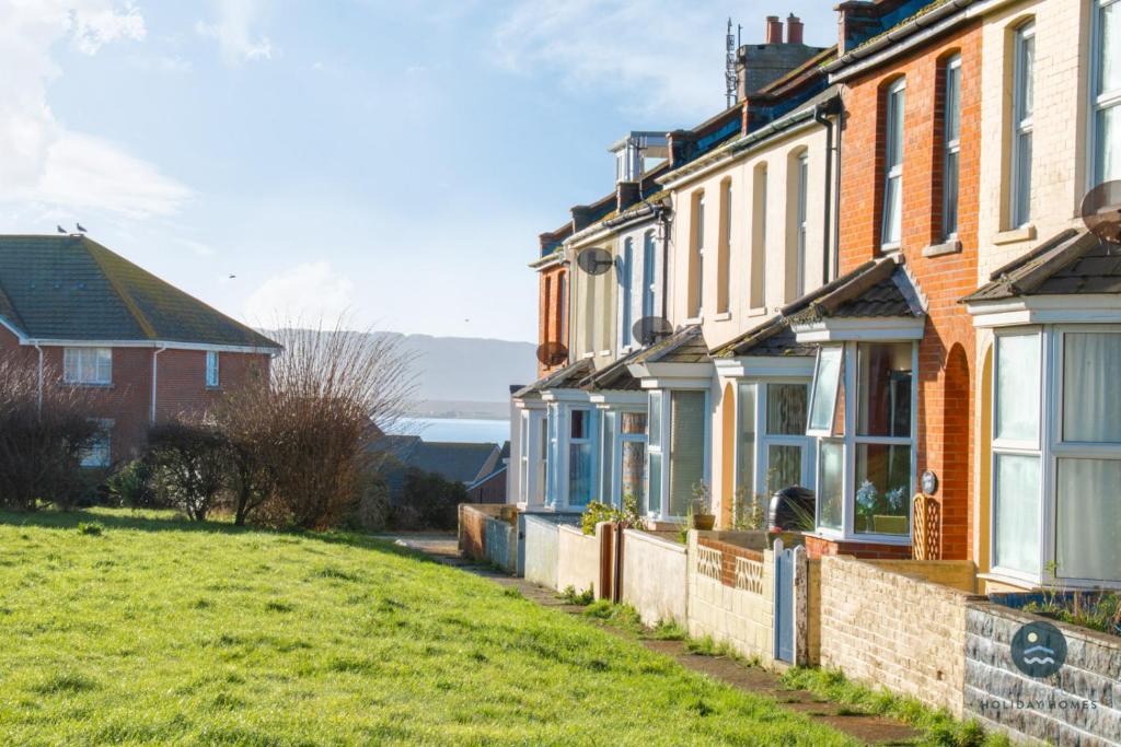 a brick house with blue windows on a green field at Spindrift - views of Chesil beach dog friendly in Weymouth