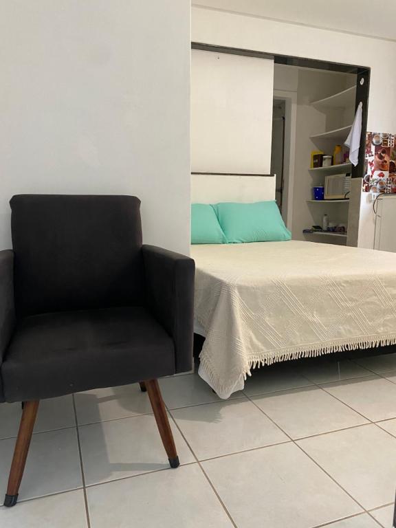 um quarto com uma cama e uma cadeira preta em Quarto e sala pé na areia em Guarapari
