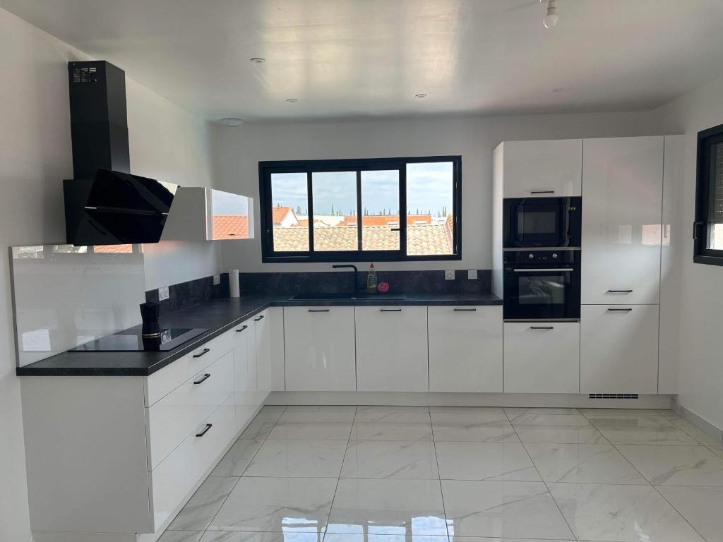 une cuisine avec des armoires blanches et une fenêtre dans l'établissement Appartement + piscine et extérieur, à Rivesaltes