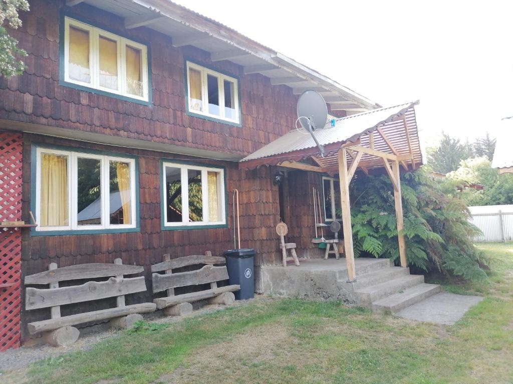 Casa de madera con porche y bancos delante en Cabañas Buen Recuerdo en Puyehue