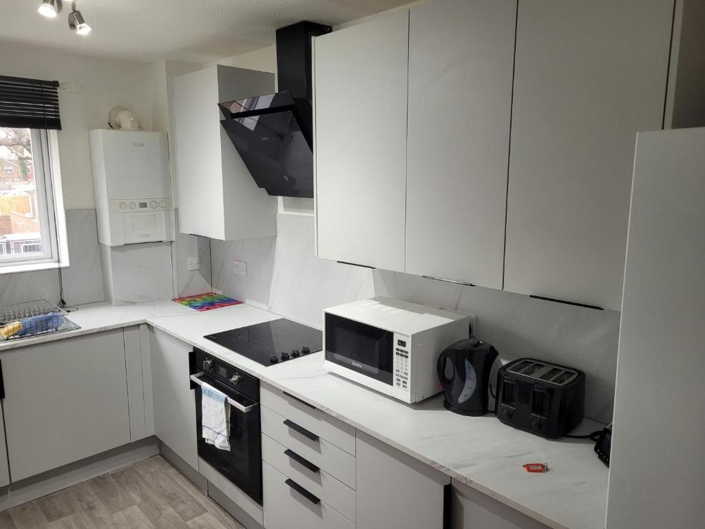 a kitchen with white cabinets and a microwave at RentUnique Nimrod House 2 bed ample parking in Crawley