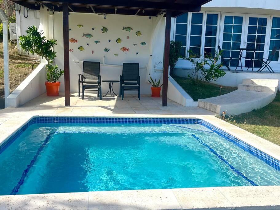 a swimming pool in front of a house with a table and chairs at Bacolet Beach House- 5 Bedrooms/ 5 Bathrooms in Bacolet