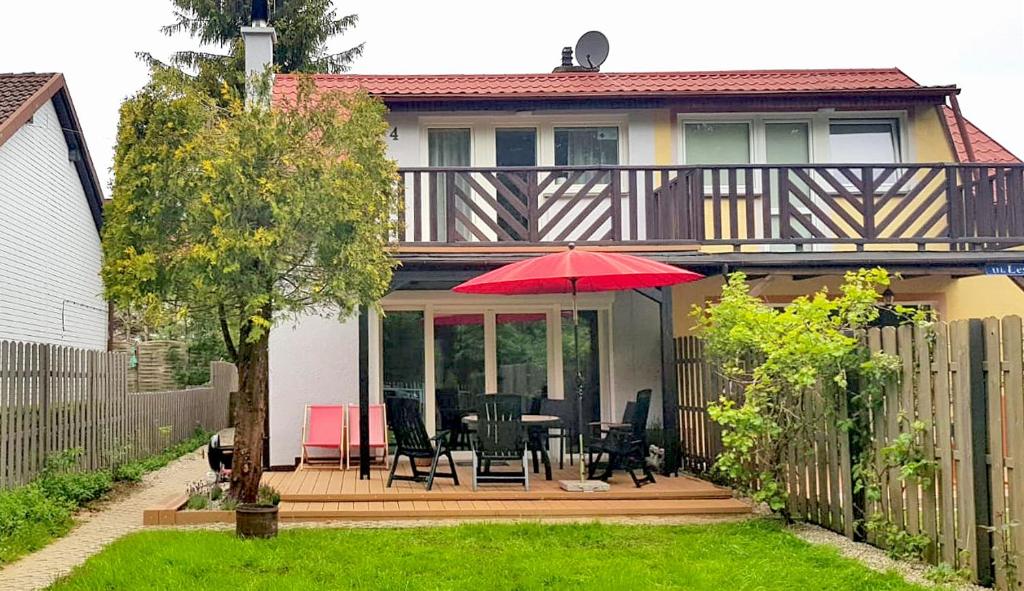 a house with a deck with a table and a red umbrella at Domek Leśny in Poddąbie