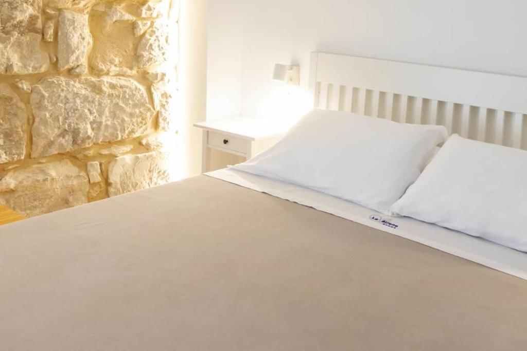 una camera con un letto bianco e un muro in pietra di Le Sirene B&B a Ragusa