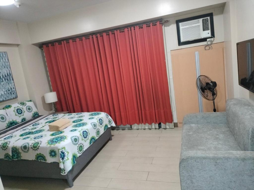 een slaapkamer met een bed en een bank en een rood gordijn bij Rqui CondoTel Near Airport in Manilla