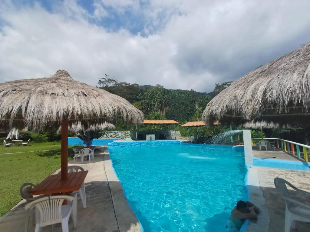 a resort with a swimming pool with a thatch roof at Cabaña rodeada de naturaleza in Cocorná