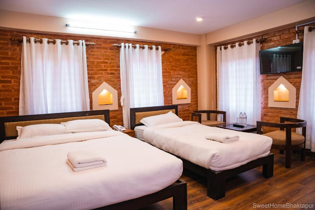 two beds in a room with two tables and windows at Sweet Home Bhaktapur in Bhaktapur