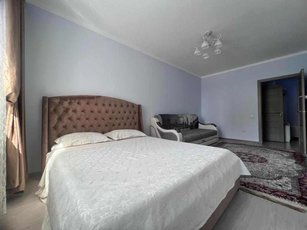 een witte slaapkamer met een groot bed en een stoel bij Апартаменты напротив спорткомплекса Алматы Арена 81-29 in Alma-Ata
