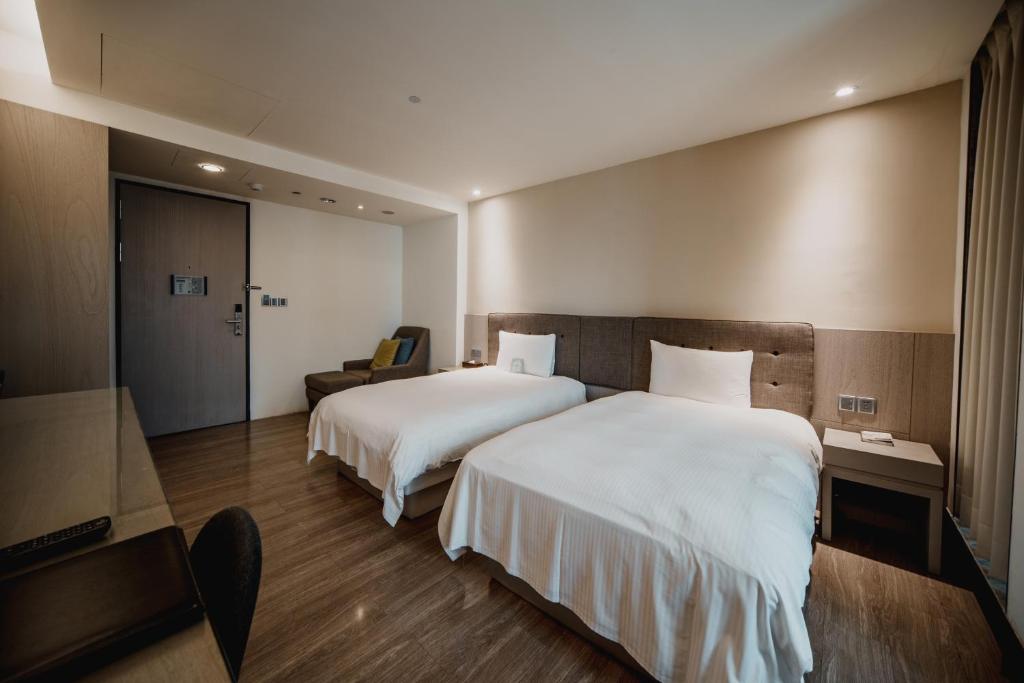 a hotel room with two beds and a chair at Hub Hotel Kaohsiung Yawan Branch in Kaohsiung