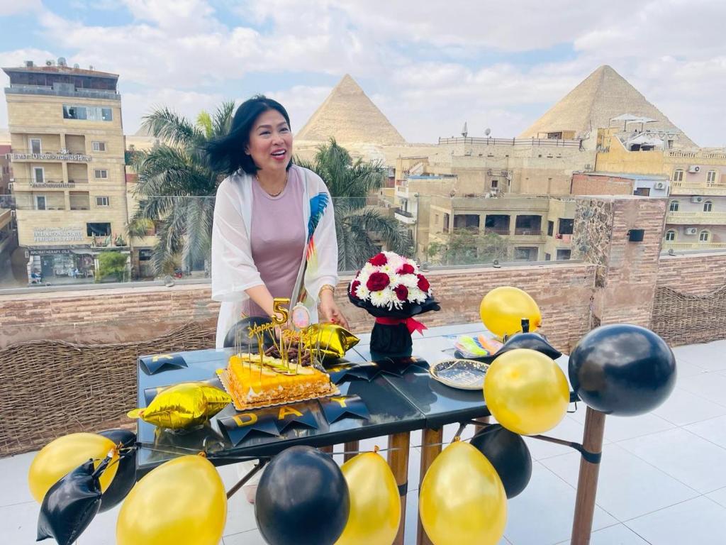 Pyramids Paradise View Inn Hotel في القاهرة: امرأة تقف أمام طاولة مع كعكة