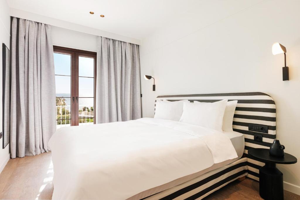 a white bedroom with a large bed and a window at Doryssa Lithos Hotel in Pythagoreio