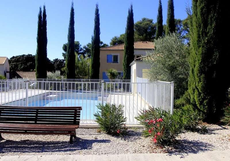 eine Bank vor einem Zaun neben einem Pool in der Unterkunft Maison calme + piscine + pinède + parking in Castries