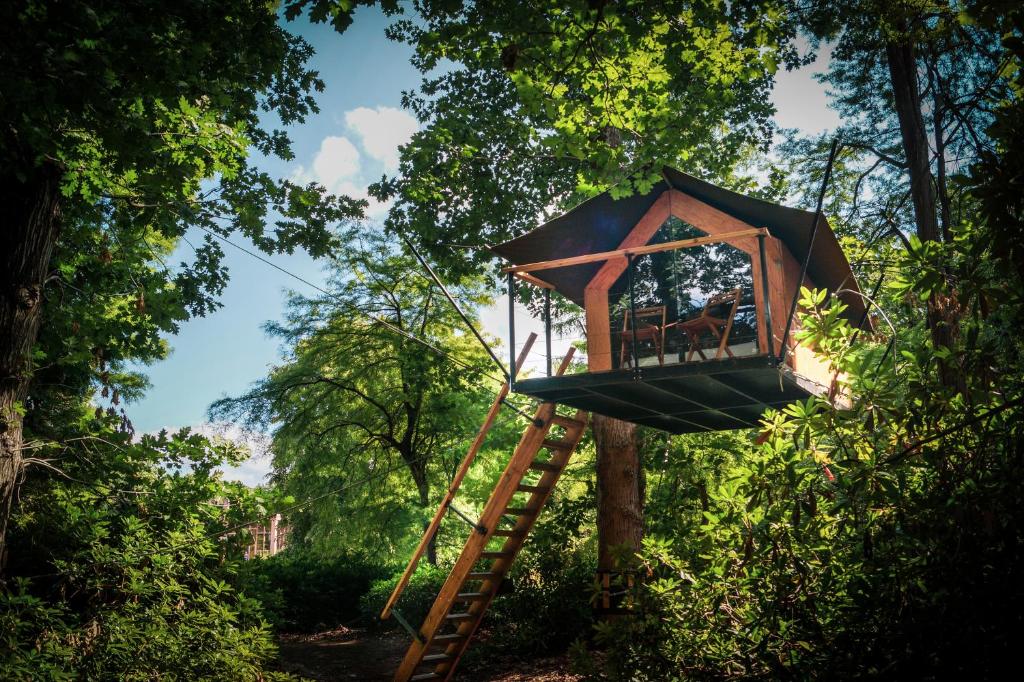 uma casa na árvore com uma escada e um guarda-chuva em Boomkamp treehouses em Oostkamp
