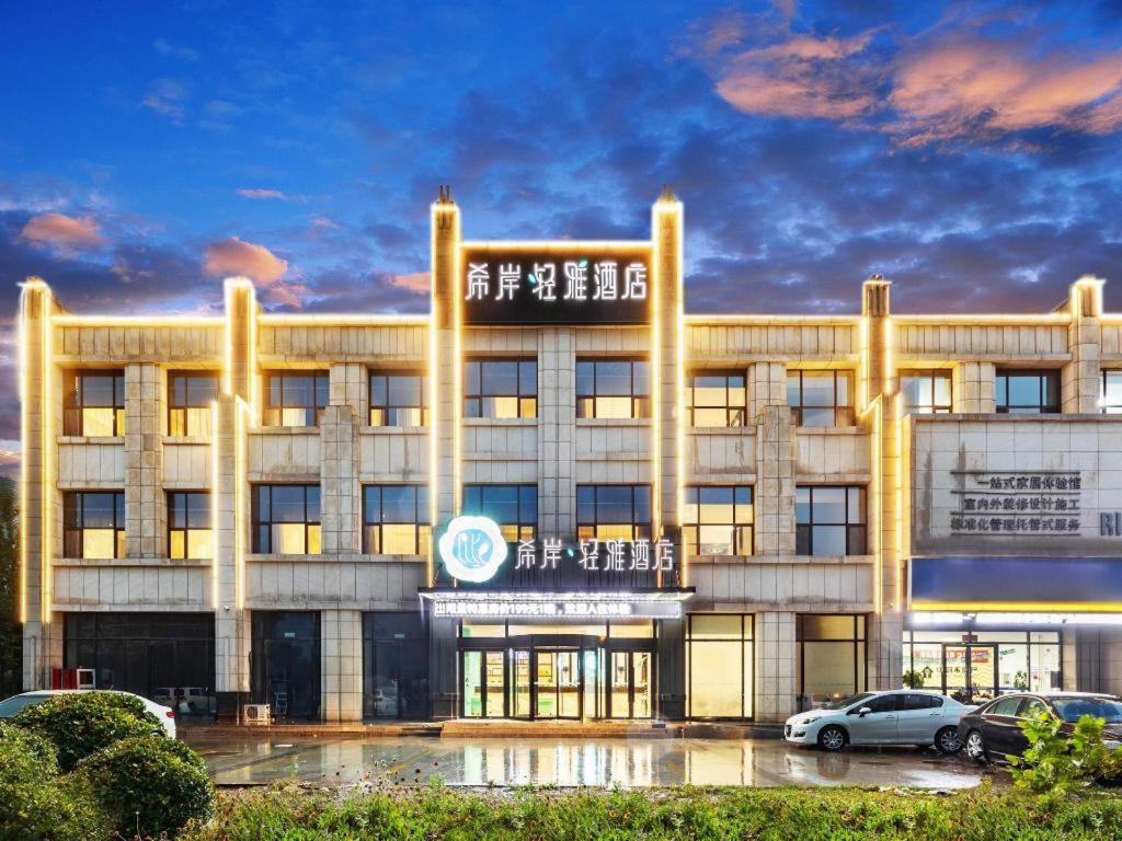 een groot gebouw met auto's geparkeerd op een parkeerplaats bij Xana Lite Tianjin Ninghe Trade Development Zone in Ninghe