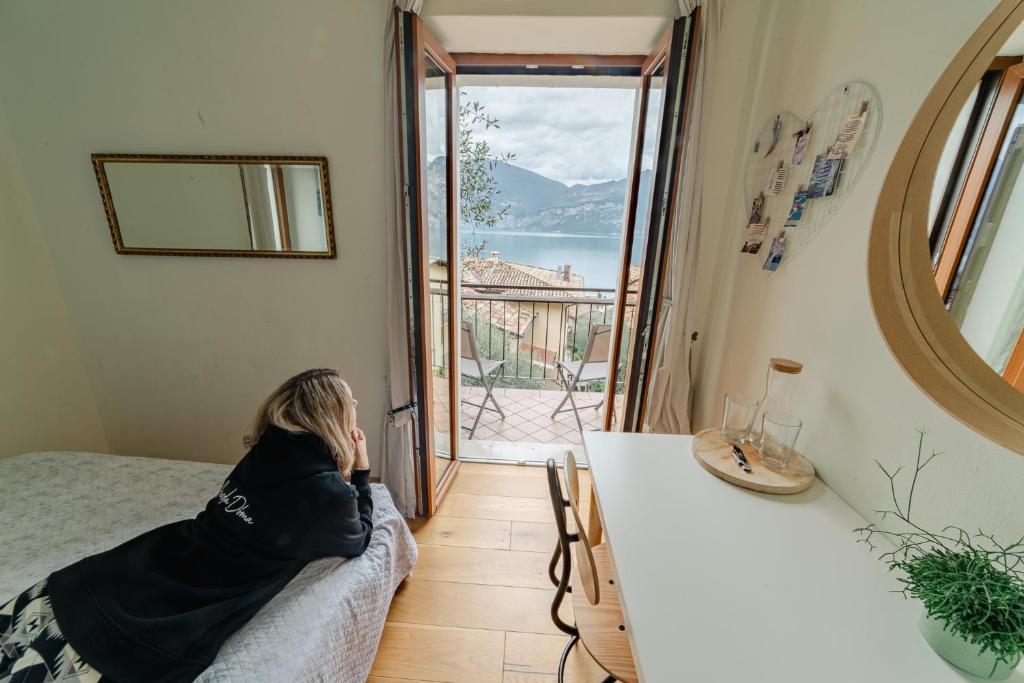 une femme assise sur un canapé dans une pièce avec vue sur un balcon dans l'établissement Garda Doma, à Brenzone