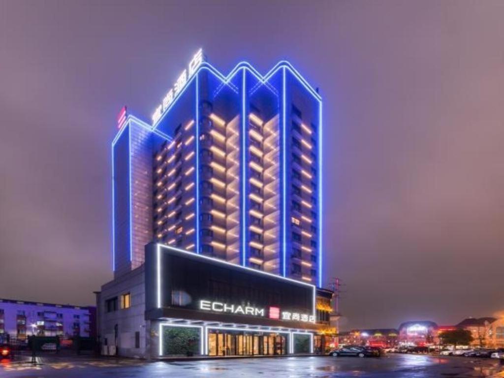 un edificio iluminado con un hotel por la noche en Echarm Hotel Huzhou Wuyue Plaza Children's Clothing City en Jijiawan