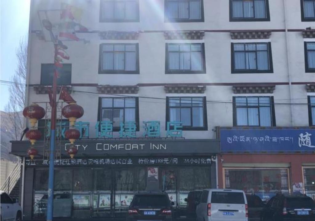 wysoki biały budynek z samochodami zaparkowanymi przed nim w obiekcie City Comfort Inn Lhasa Gongga County Gongga Airport 