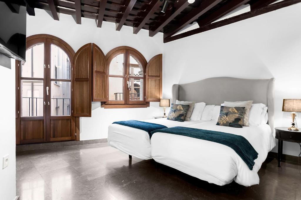 a bedroom with a large white bed and windows at Hotel Mercader de Sedas in Granada