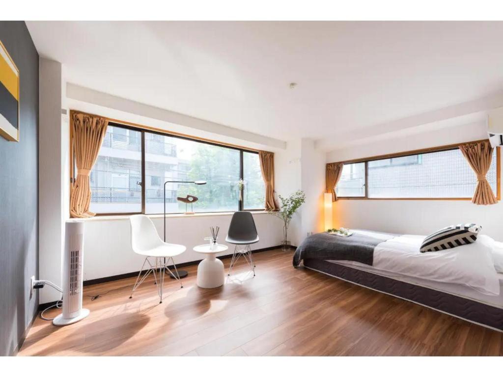 a bedroom with a bed and two chairs and windows at Tora Hotel Rikugien in Tokyo