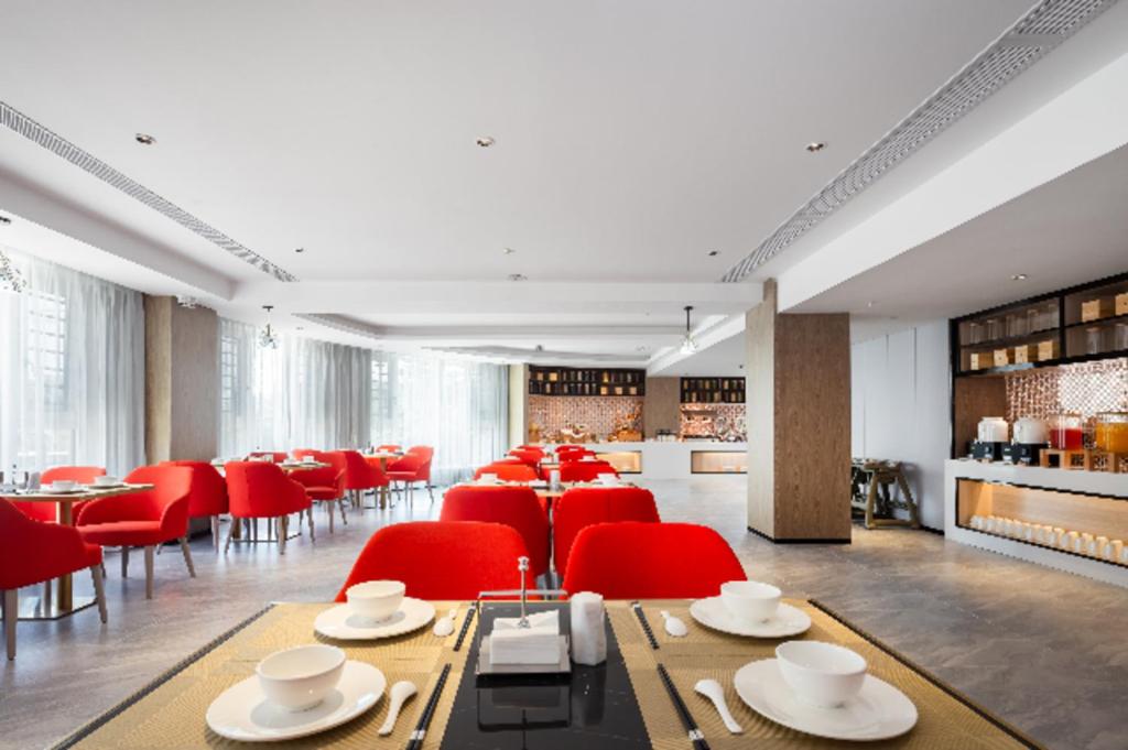 uma sala de jantar com cadeiras vermelhas e mesas num quarto em Echarm Hotel Haikou Yehai Avenue Airport em Lingshan