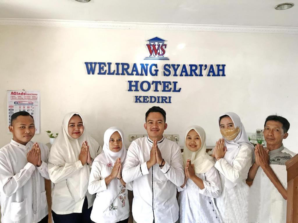a group of people dressed in white praying in front of a sign at Hotel Welirang Syariah in Kediri