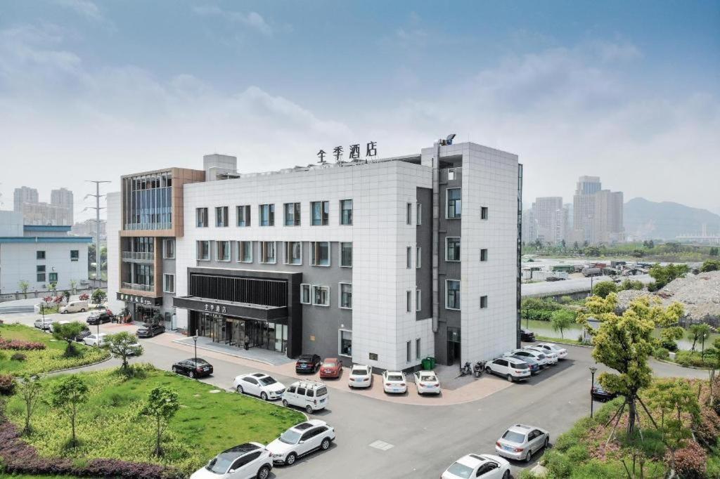 a large white building with cars parked in a parking lot at JI Hotel Wenzhou South Railway Station in Louqiao