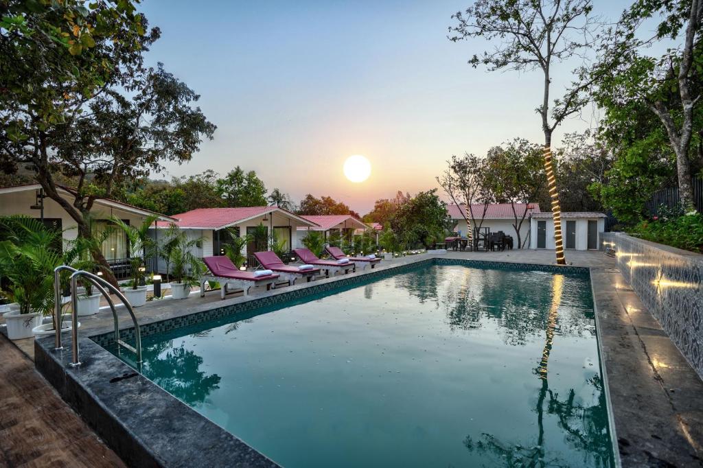 ein Pool mit Stühlen und der Sonnenuntergang im Hintergrund in der Unterkunft Amore Serenity Resort in Arambol
