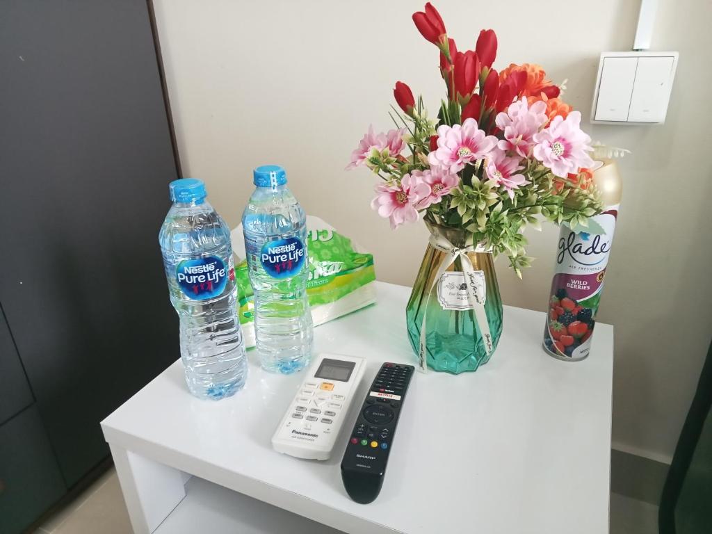 バタム・センターにあるApartement Studio Pollux Habibi Batam A13712のテーブル(リモコン付)、ボトル入り飲料水2本、花