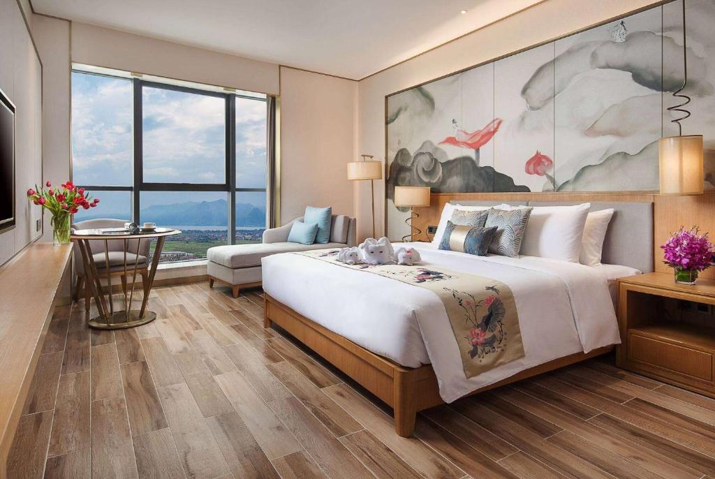 um quarto com uma grande cama branca e uma mesa em Ramada Plaza Fuxian Lake em Chengjiang