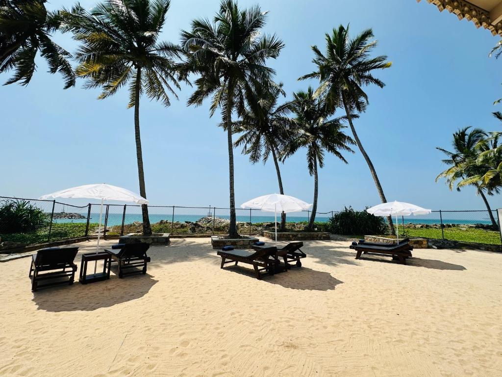 a sandy beach with tables and umbrellas and palm trees at Moi Hikka by DBI in Hikkaduwa