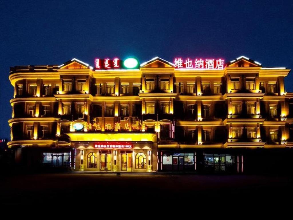 Vienna Hotel Inner Mongolia Tongliao Development Zone في تونغلياو: مبنى مضاء في الليل مع ضوء أخضر