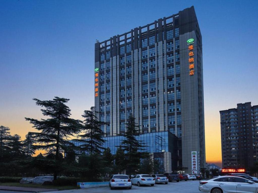 a tall building with cars parked in a parking lot at Vienna Hotel Shandong Liaocheng High-Tech Zong Yueji Park in Liaocheng