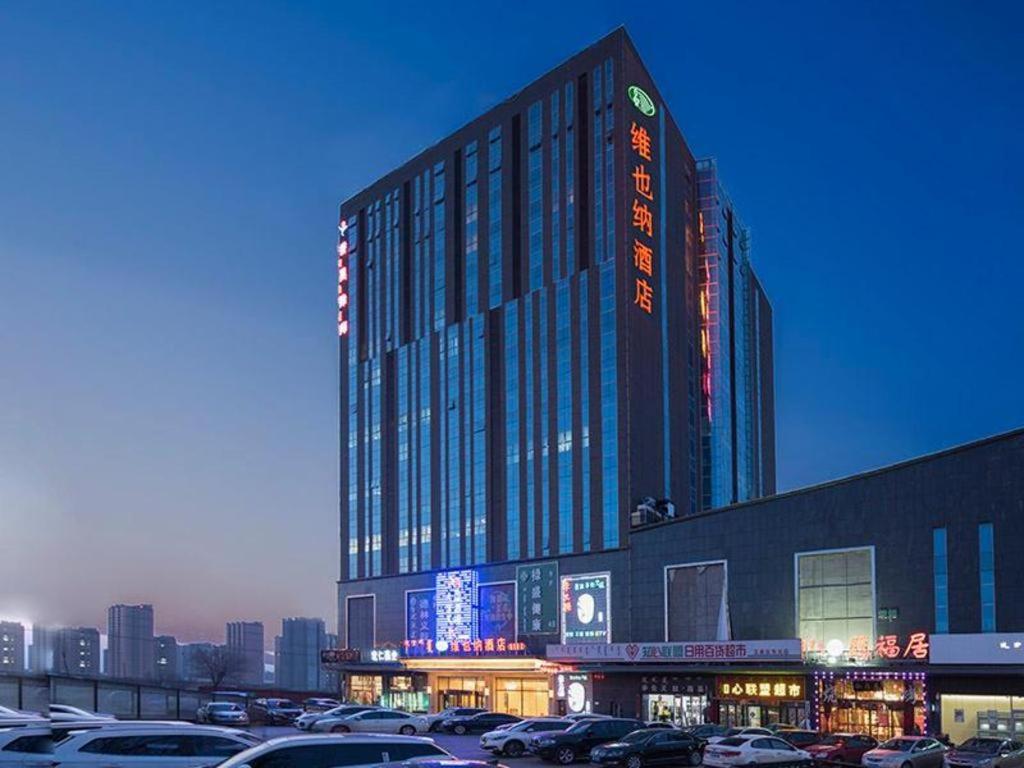 duży budynek z samochodami zaparkowanymi na parkingu w obiekcie Vienna Hotel Hohhot Zhaojun Road w mieście Hohhot