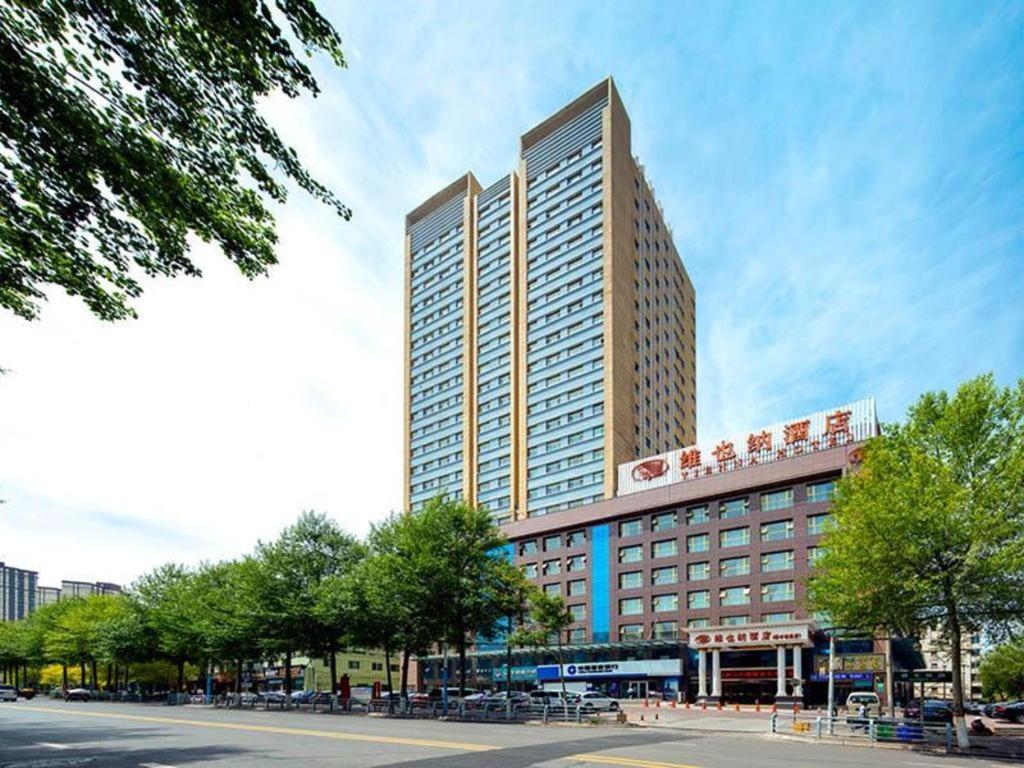 西寧市にあるVienna Hotel Qinghai Xining Deling Halu City East Wanda Plazaの木立の大きな高層ビル