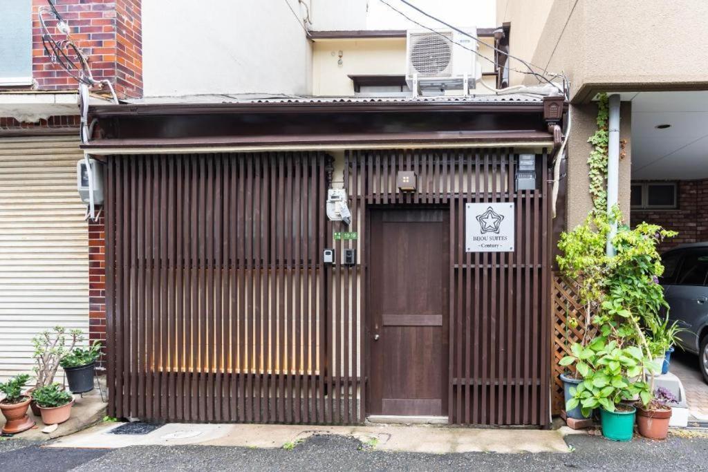 un edificio con una puerta de madera con plantas alrededor en Bijou Suites Century en Osaka