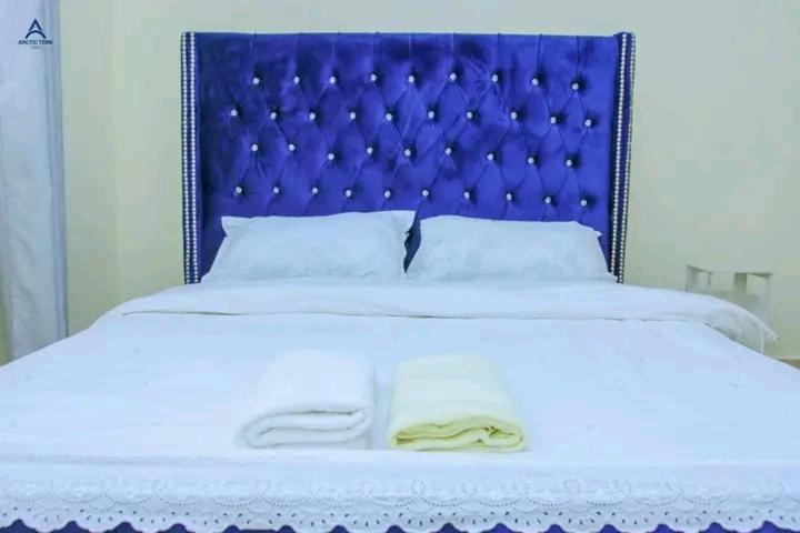 a bed with a blue headboard and white sheets and pillows at Arctic kerugoya in Keruguya
