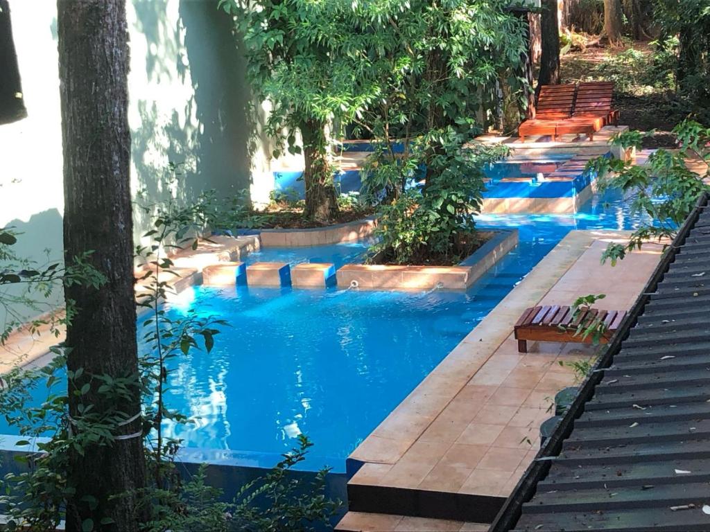 una piscina con agua azul, árboles y bancos en Kelta Hotel Puerto Iguazú CENTRO en Puerto Iguazú